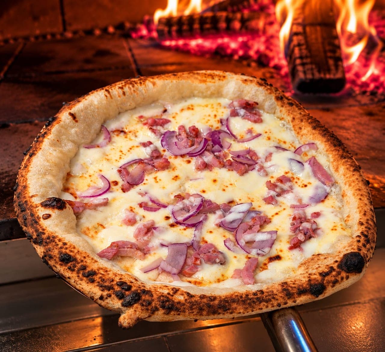 La pizza Alsacienne sur la pelle, devant les flammes du four à bois.