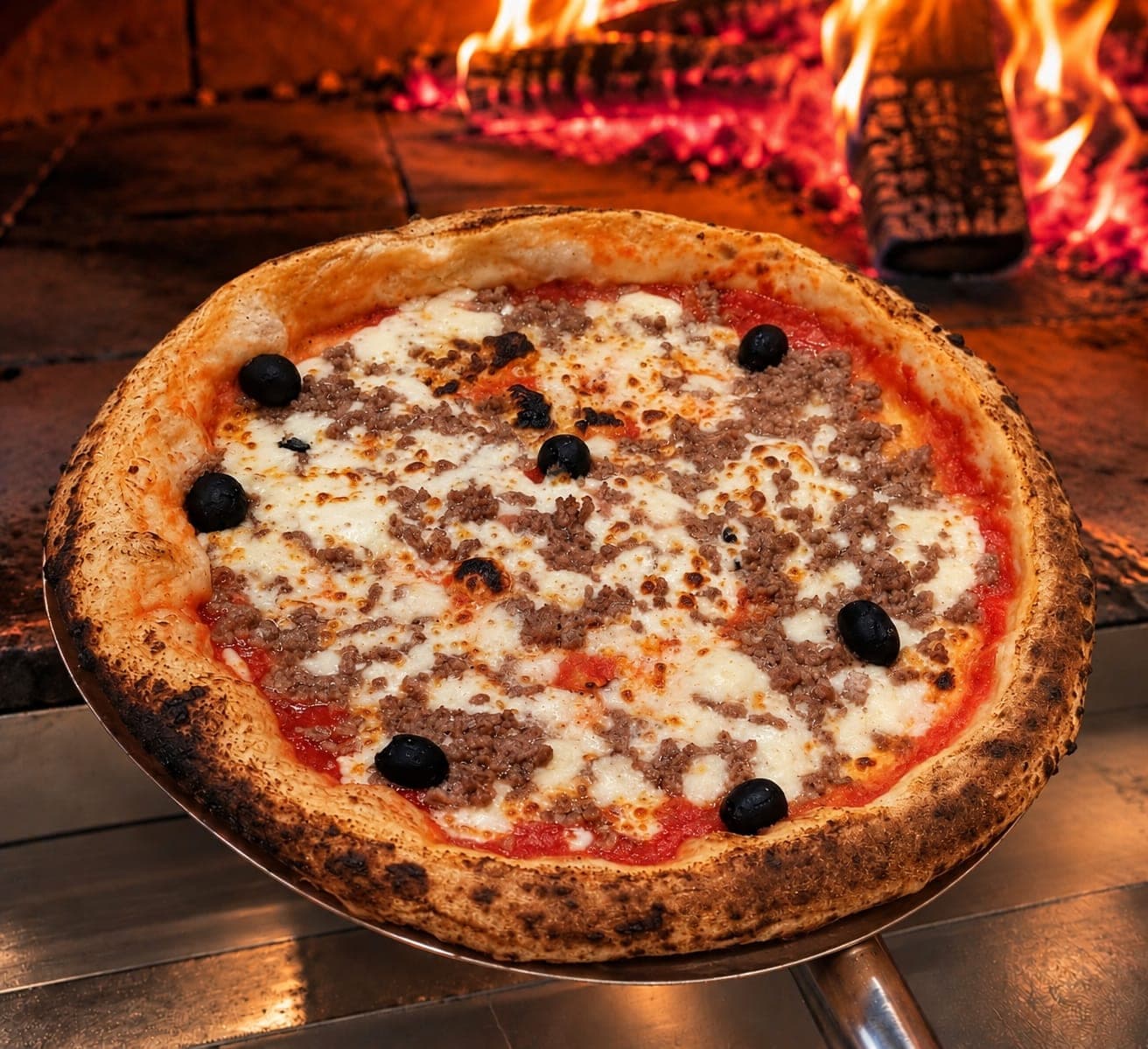 La pizza Bolognaise sur la pelle, devant les flammes du four à bois.