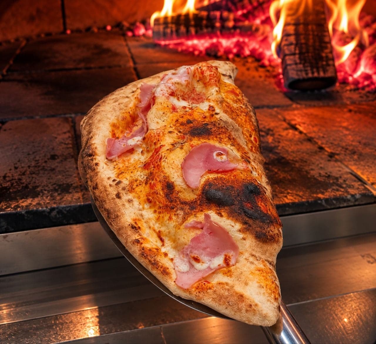 La pizza Calzone sur la pelle, devant les flammes du four à bois.