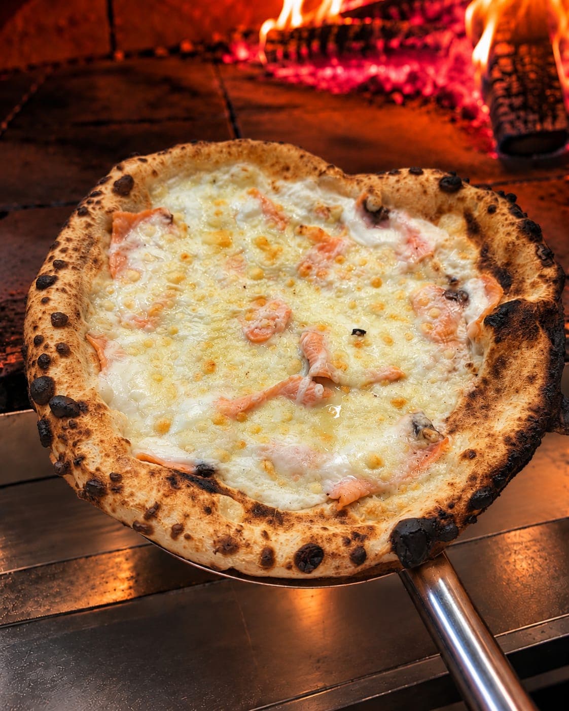La pizza Pacifique sur la pelle, devant les flammes du four à bois.