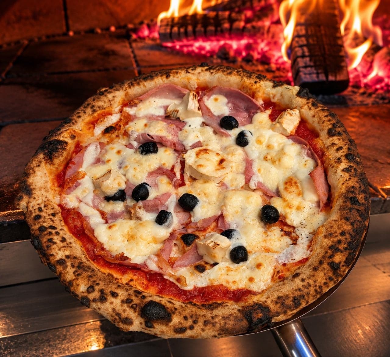 La pizza Parme sur la pelle, devant les flammes du four à bois.