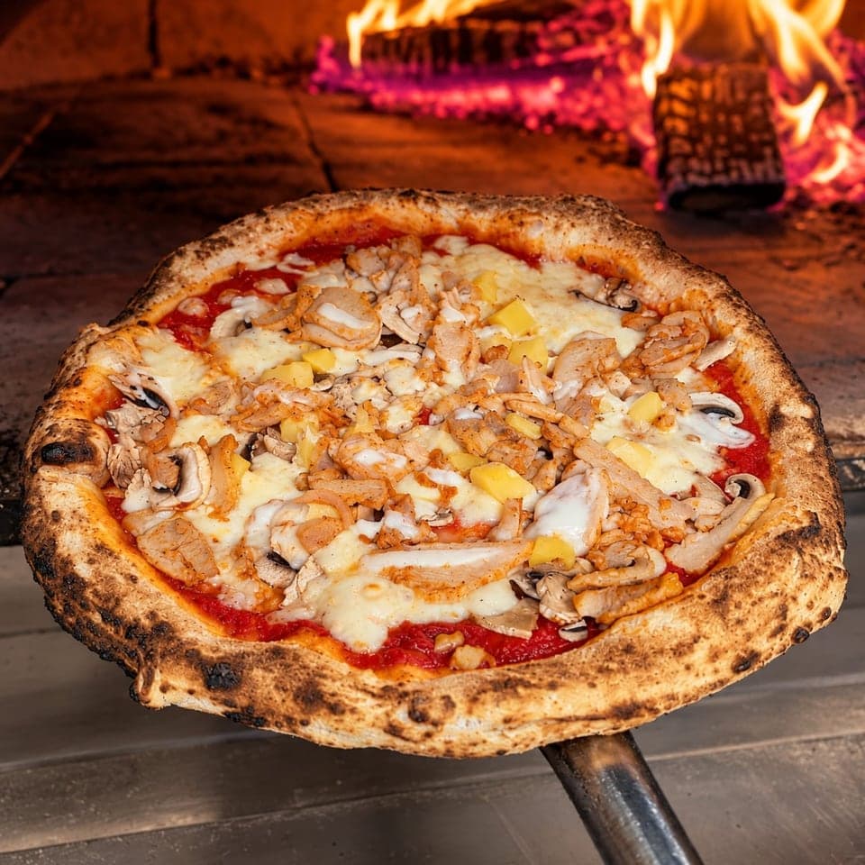 La pizza Poulet sur la pelle, devant les flammes du four à bois.