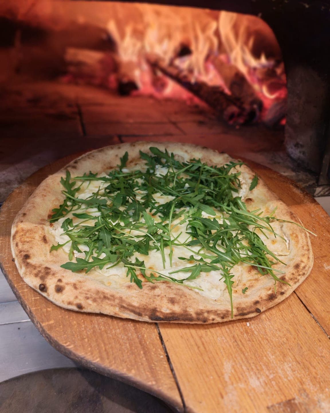La pizza Rose sur la pelle en bois, devant les flammes du four à bois.