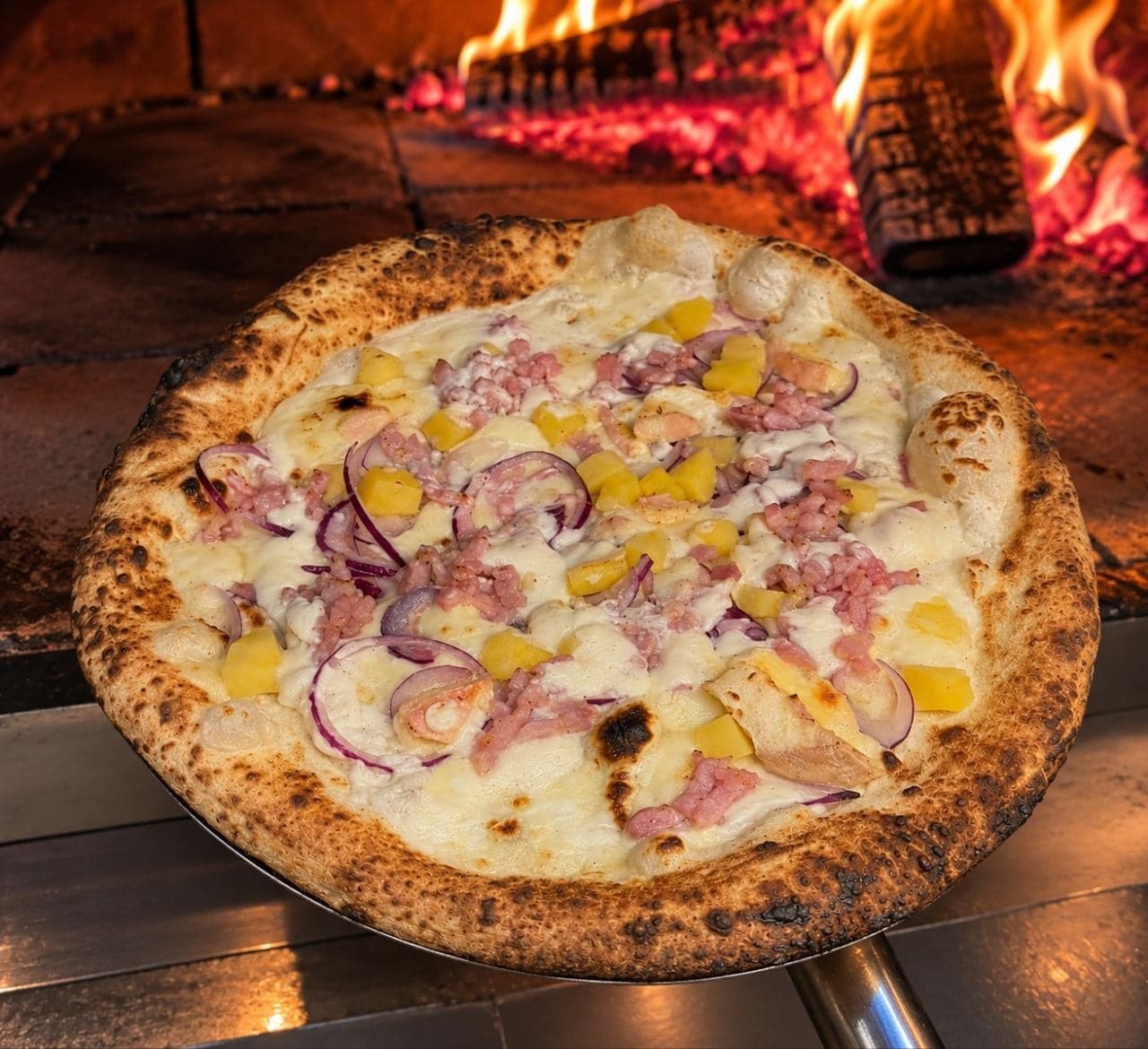 La pizza Tartiflette sur la pelle, devant les flammes du four à bois.